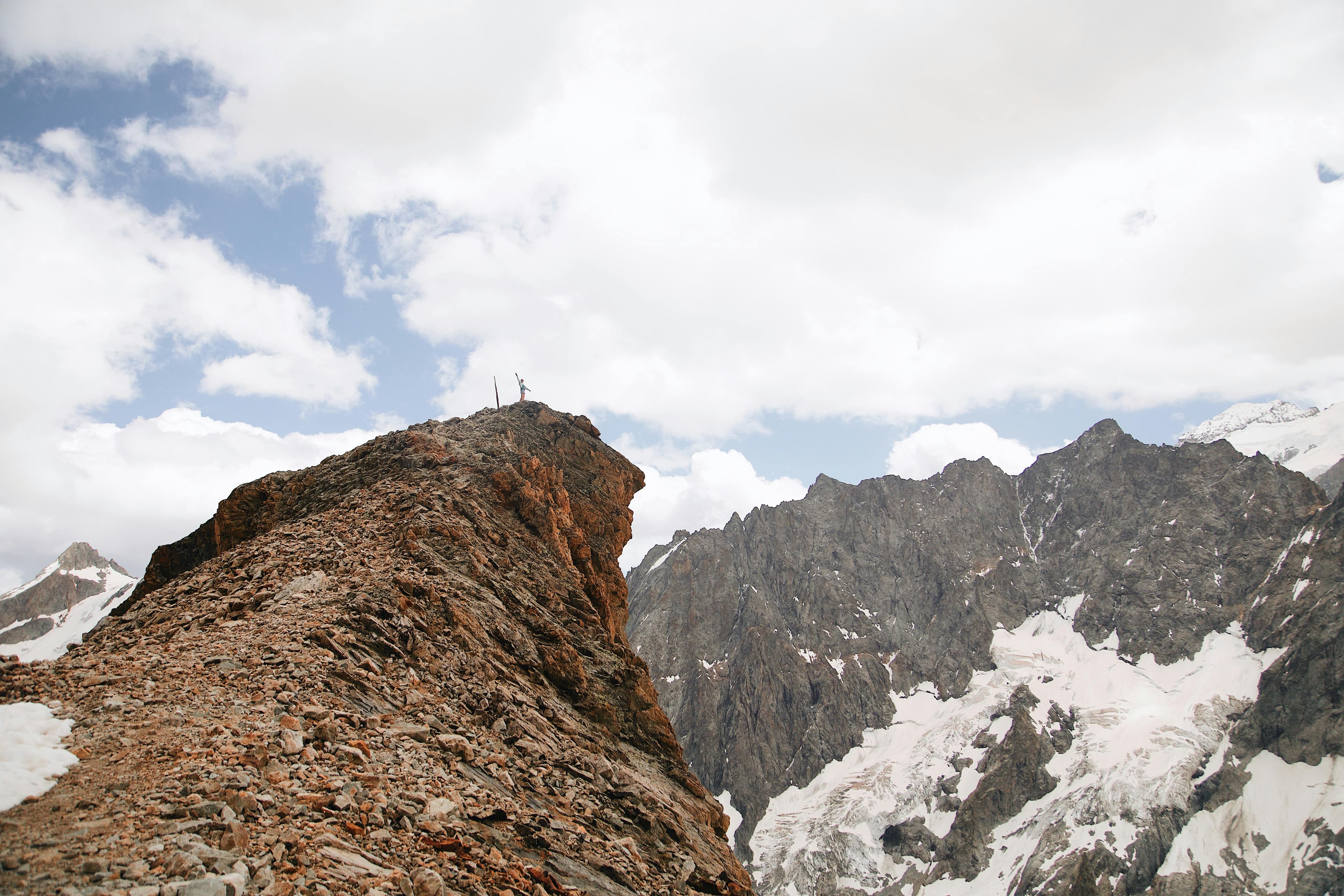 A person standing on a rocky summit above mountain peaks